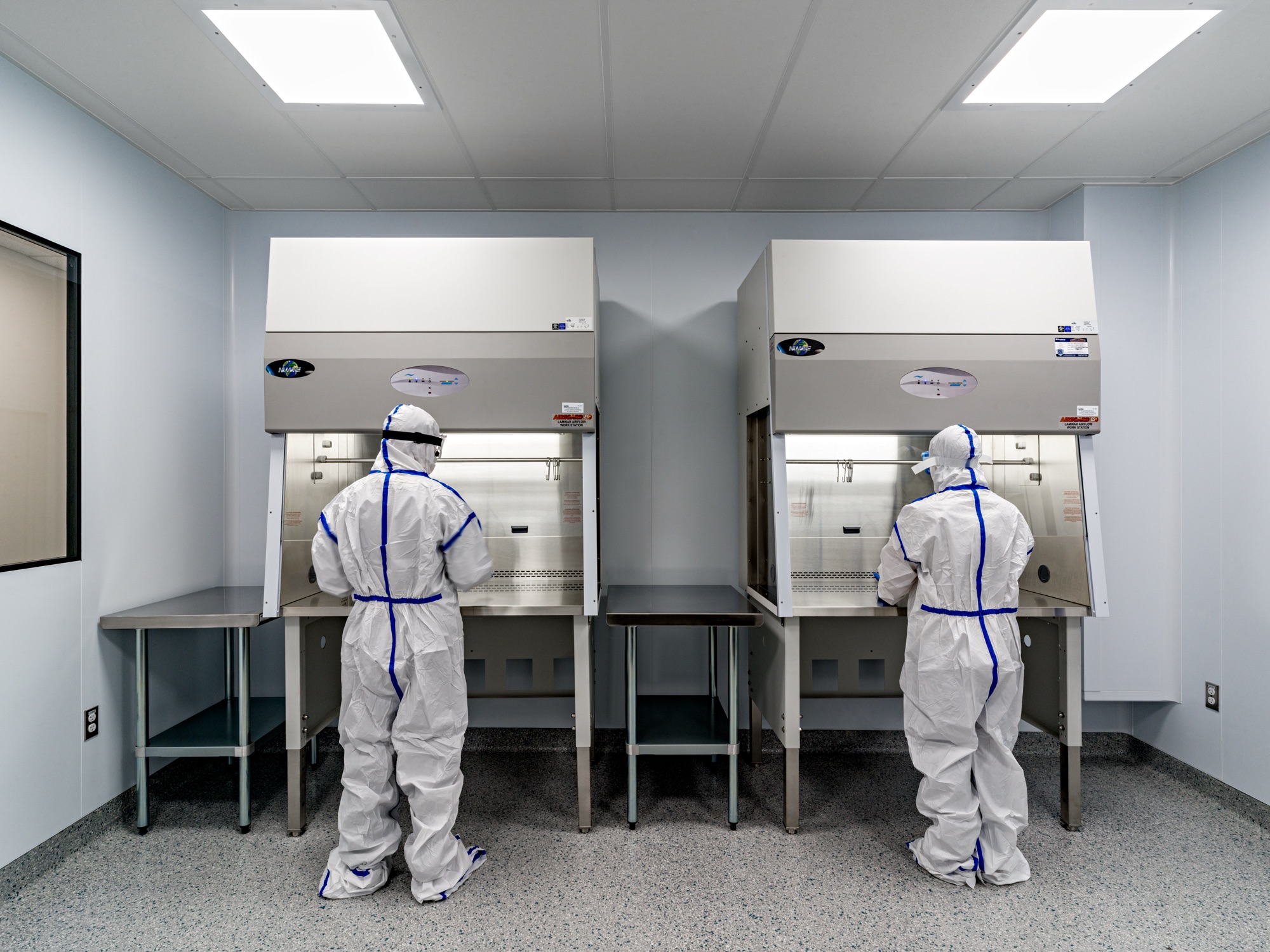 Two compounding technicians in sterile garb working at the laminar-flow hoods in the AOM cleanroom