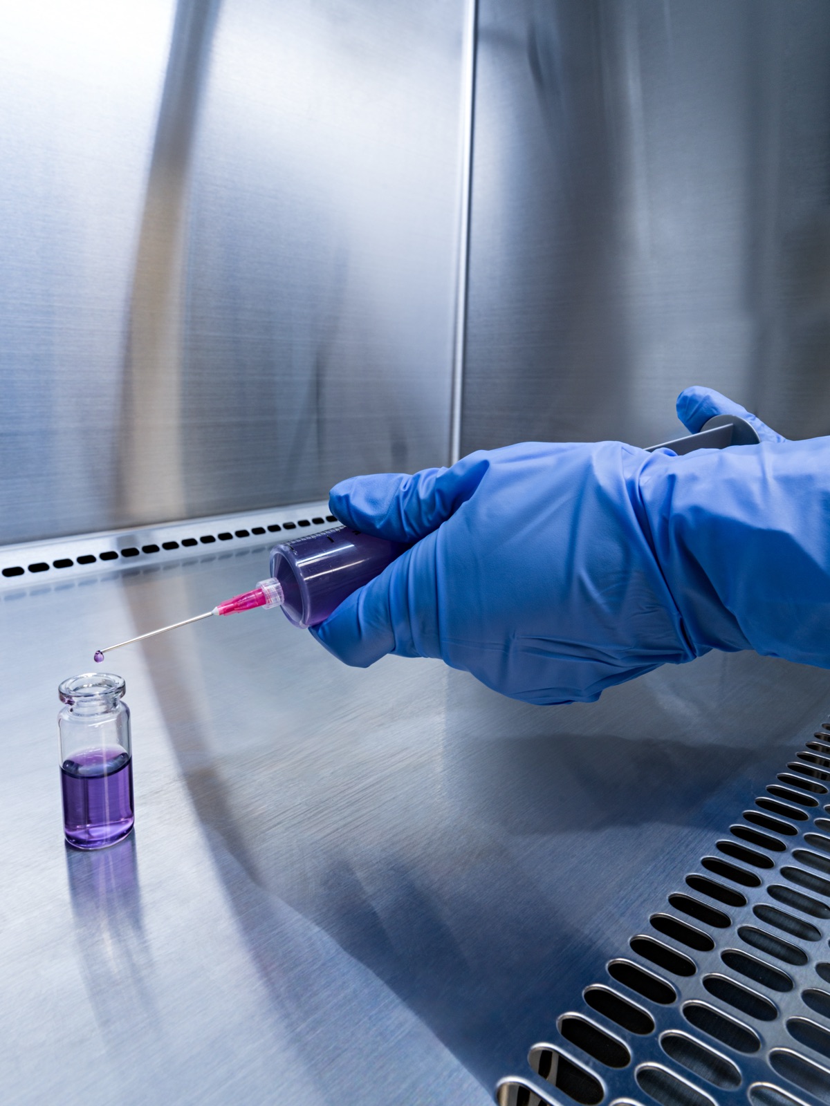 Gloved hands drawing a compounded solution into a syringe inside the sterile hood